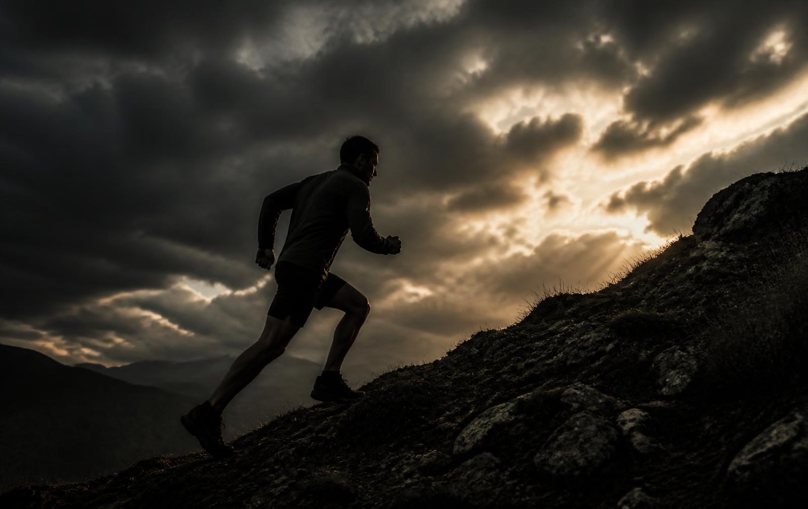 Man running up a rocky hill at dawn under storm clouds